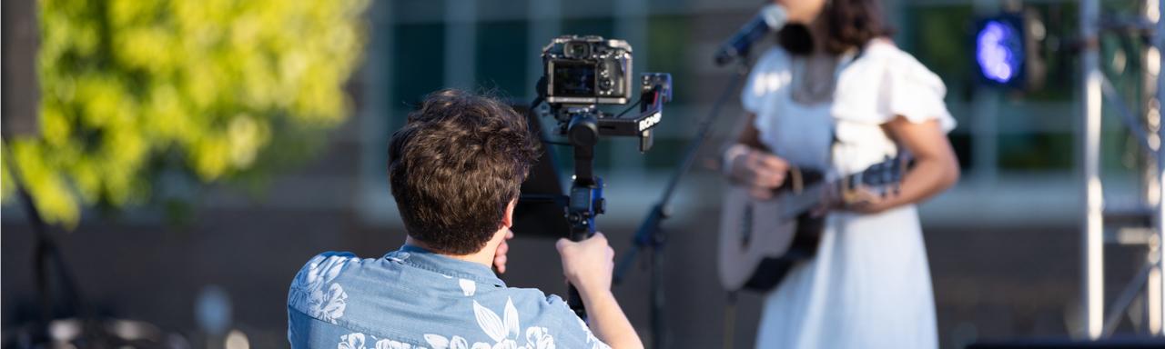 A student filming another student singing and playing the guitar onstage